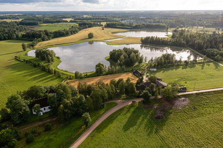 Expansive green meadows and calm lakes create a peaceful rural setting under a cloudy sky.の写真素材