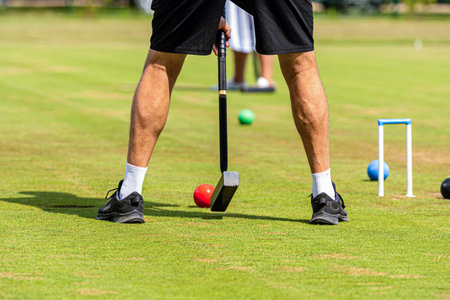 A player prepares to strike a red croquet ball on a well-maintained grassy field.の写真素材