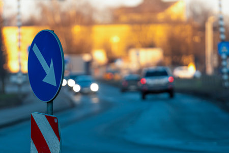 Cars driving along a road while a directional traffic sign stands prominently in the foregroundの写真素材