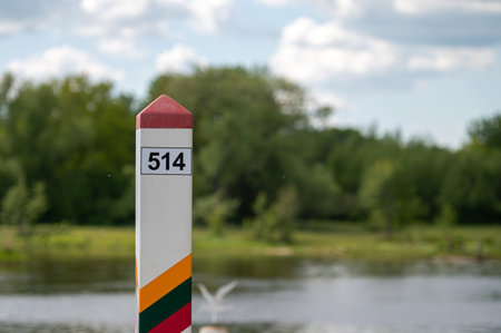 Border marker indicating Lithuania along a serene river under a partly cloudy skyの写真素材
