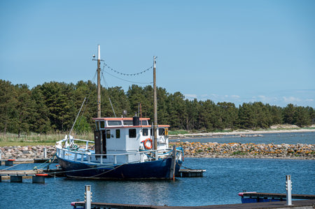 A fishing boat rests at a dock near a tranquil shoreline under a clear blue sky.の写真素材