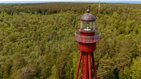 Ruhnu lighthouse stands tall in Estonia, overlooking a dense forest and the serene sea.の写真素材