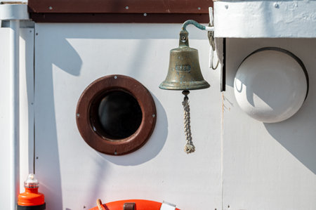A brass bell hangs by a round porthole, highlighting nautical design and textures.の写真素材