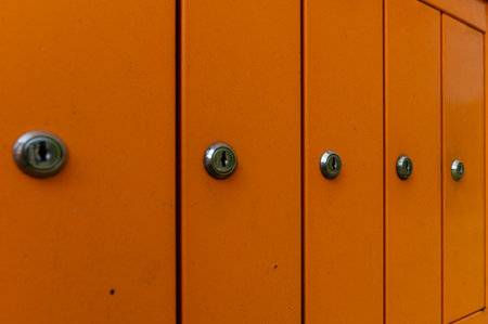 Rows of bright orange mailboxes with shiny locks stand in a city area under clear skies.の写真素材