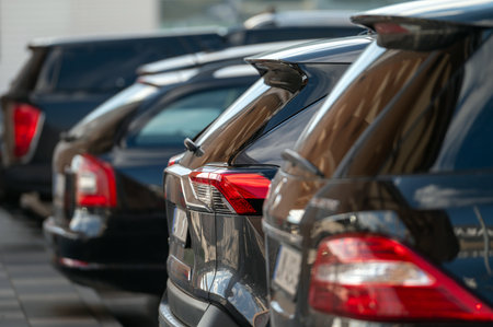 Several black cars are neatly parked in a row, reflecting sunlight in an urban area.の写真素材
