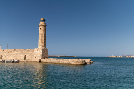 Lighthouse marks the entrance to the harbor under the bright blue sky in Rethymno, Crete.の写真素材
