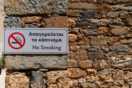 A no smoking sign displayed on a textured stone wall under bright sunlightの写真素材