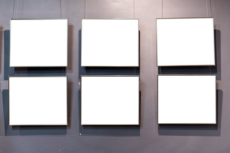 Six empty picture frames are displayed against a gray wall, hanging by clear wires.の写真素材