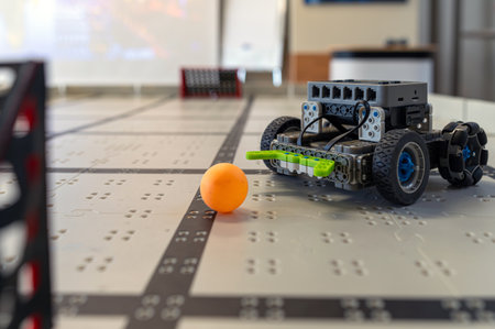 A small robot navigates a table while targeting an orange ball in a tech workshop.の写真素材