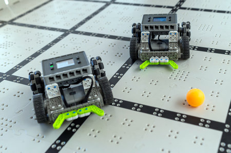 Two robots navigate a grid-based arena while trying to interact with a small ball.の写真素材