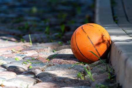 Orange basketball lies on a cobblestone surface with green grass around in sunny weather.の写真素材