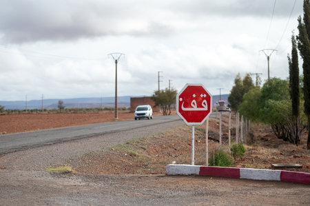 Arabic stop sign visible beside a rural road in Morocco with a car approaching in the distance.の写真素材