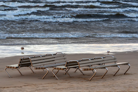 Benches by the shore at sunset with gentle waves lapping against the sand