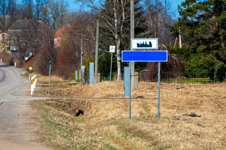 A road sign stands next to a rural road with grassy areas and trees in the background.の写真素材