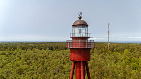 Tall red lighthouse overlooks vibrant forests and coastline on Ruhnu Island in Estonia.の写真素材