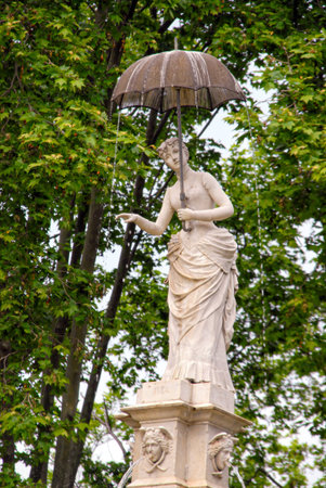 Barcelona, Spain - April 30, 2009: A statue holds an umbrella while rain falls in a park in Barcelona surrounded by trees.のeditorial素材
