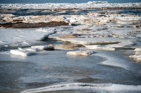 Ice spreads across a water surface with melting patches showing the land underneath