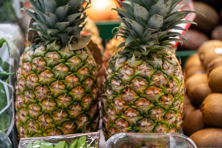 Two pineapples sit among various fruits at a market stall in the afternoon.