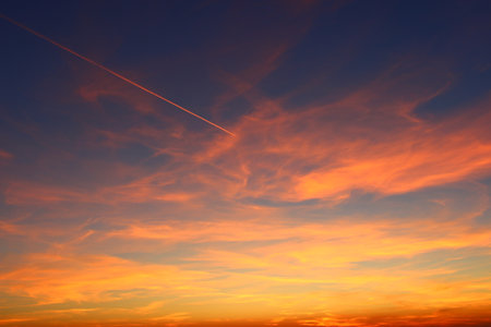 airplane and its trail in the sky. clouds and different color tones in the sky at sunset. Amazing and incredible sunset.の写真素材