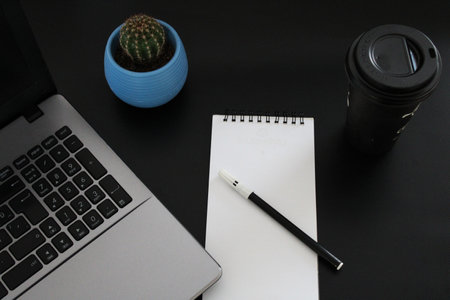 Blank notebook with pen are on top of wood office desk table with a cup of coffee and office...