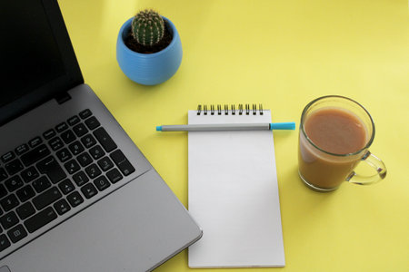 Blank notebook with pen are on top of wood office desk table with a cup of coffee and office...