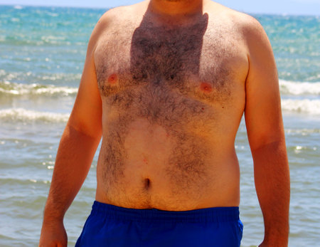 Extremely hairy body of a fat man on sea background.の写真素材
