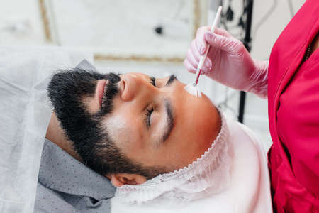 A young man is undergoing a cosmetic facial peeling procedure. Cosmetology and rejuvenation