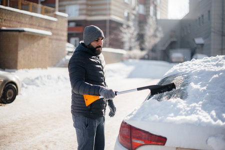 A young man cleans his car after a snowfall on a sunny, frosty day.の写真素材