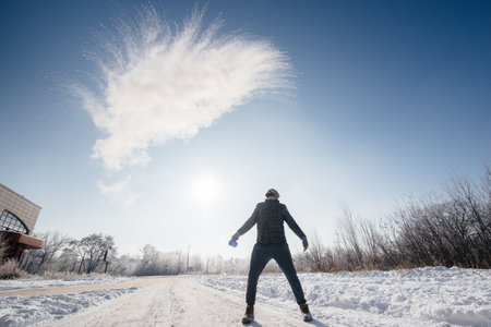 A man throws out boiling water in the cold, which instantly turns into steam. The hot water trick.の写真素材