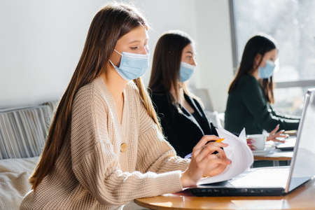A group of masked girls keep a social distance in a cafe when working on laptops.の写真素材