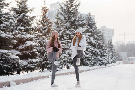 Two young athletic girls do a warm-up before running on a sunny winter day. A healthy way of life.