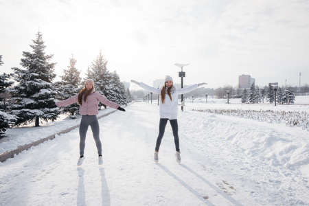 Two young athletic girls do a warm-up before running on a sunny winter day. A healthy way of life.