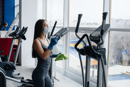 The girl in the mask disinfecting the gym equipment during a pandemic.の写真素材