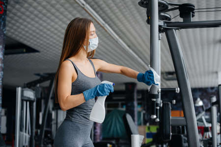 The girl in the mask disinfecting the gym equipment during a pandemic.の写真素材