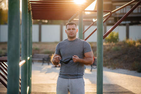 A young man does push-UPS, pull-UPS on a sports field in a mask during a pandemic at sunset. Sports,...