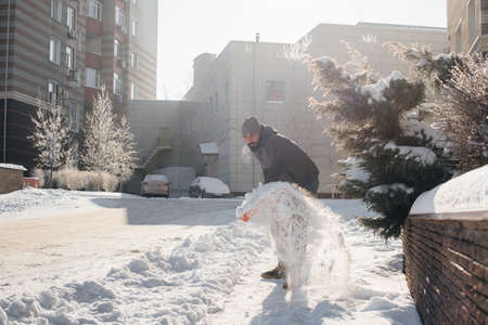 A young man clears the snow in front of the house on a sunny and frosty day. Cleaning the street from snow.の写真素材