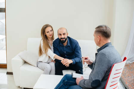 A young happy married couple of men and women talk to a psychologist at a therapy session....