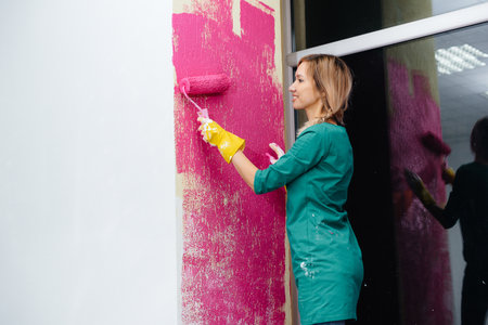 A young girl paints a white wall in pink with a roller close-up. Repair of the interior.の写真素材