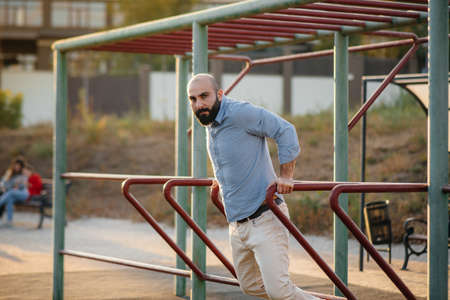 A young man with a beard performs push-ups on the uneven bars.の写真素材