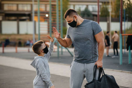 A father and child stand on a sports field in masks after training during sunsetの写真素材