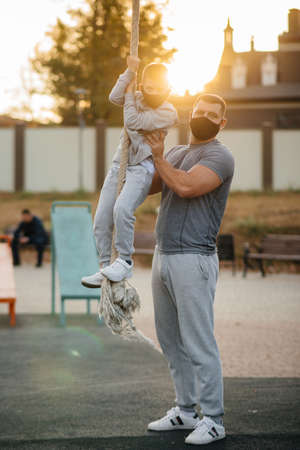 A father helps his son climb a rope on a sports field in masks during sunset. Healthy parenting and healthy lifestyleの写真素材