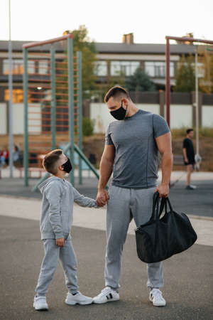 A father and child stand on a sports field in masks after training during sunsetの写真素材