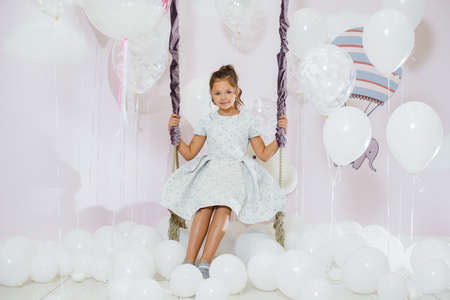 A little cute girl smiles and poses against the background of a swing with balloons.の写真素材