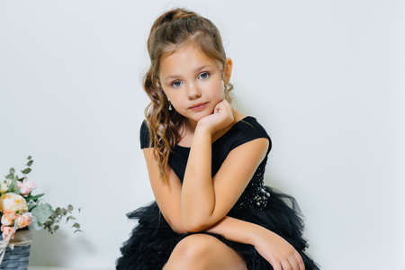 A little cute girl in a black dress is sitting and smiling with a bouquet of flowers.の写真素材