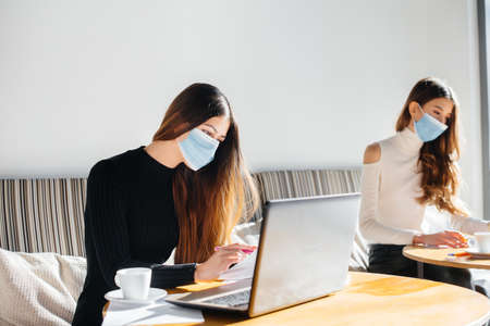 A group of masked girls keep a social distance in a cafe when working on laptops.の写真素材