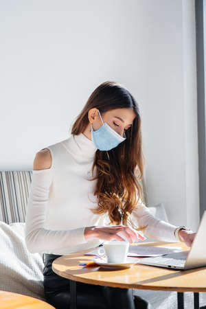 A young girl is sitting in a cafe wearing a mask and working at a computer.の写真素材