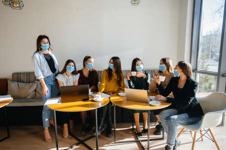 A group of girls in masks sit in a cafe and work on laptops. Teaching students.の写真素材