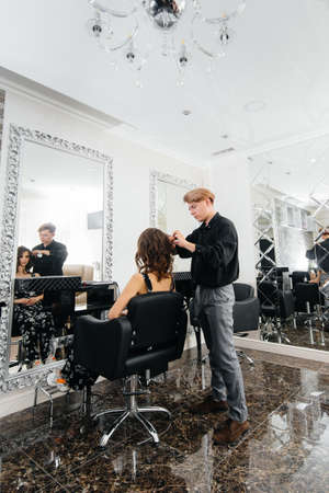 In a beautiful, modern beauty salon, a professional stylist makes a haircut and hairstyle for a young girl. Beauty, and fashionの写真素材