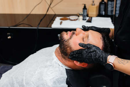 A professional stylist in a modern stylish barbershop shaves and cuts a young man's hair. Beauty salon, hair salonの写真素材