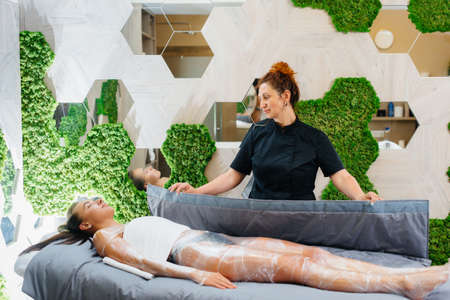 A young beautiful girl is doing a cosmetology procedure full body wrap in a modern beauty salon. Spa procedures in a beauty salonの写真素材